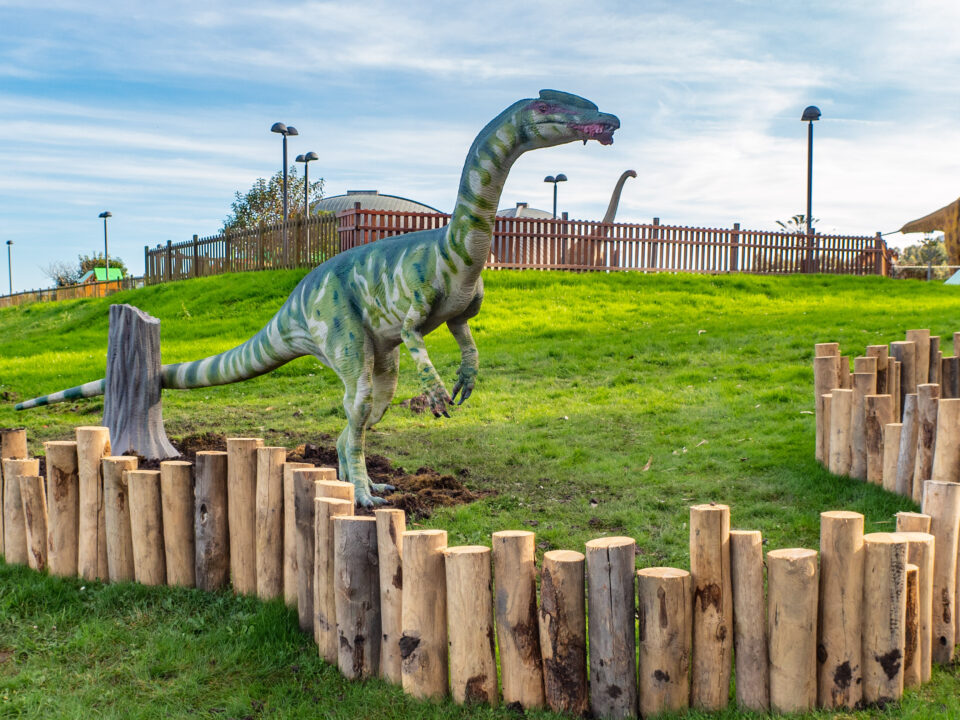 Reproducción del dinosaurio Liliensternus en el jardín exterior del Museo del Jurásico de Asturias. Es un dinosaurio terópodo (carnívoro) con un patrón de manchas de color verde, esbelto y con cresta. En la boca tiene un pedazo de carne.
